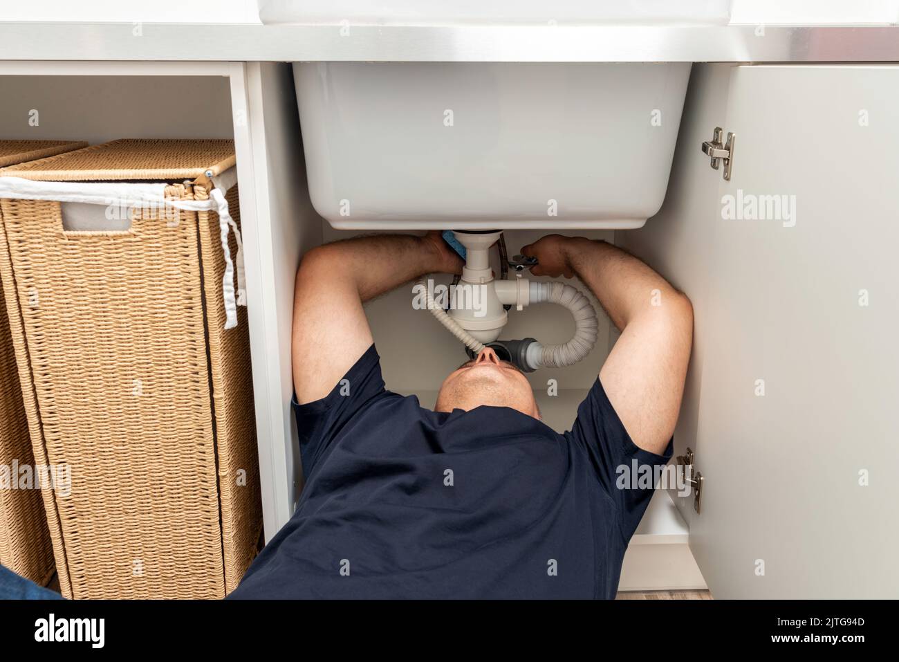 Homme dans une position difficile essayant de fixer le tuyau sous l'évier Banque D'Images