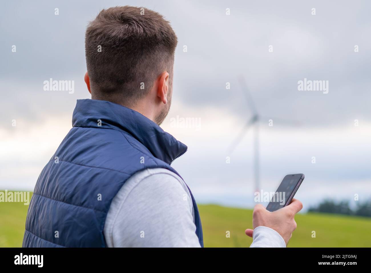 L'ingénieur utilise le téléphone portable pour vérifier le fonctionnement de l'éolienne. L'éolienne produit de l'énergie verte contre le ciel gris Banque D'Images