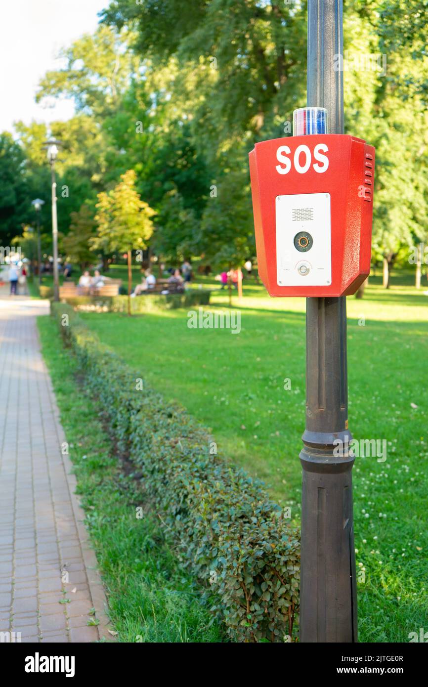 SOS, police, bouton d'urgence dans le parc public. Boîtier rouge avec caméra vidéo et voyant d'avertissement bleu sur le dessus Banque D'Images