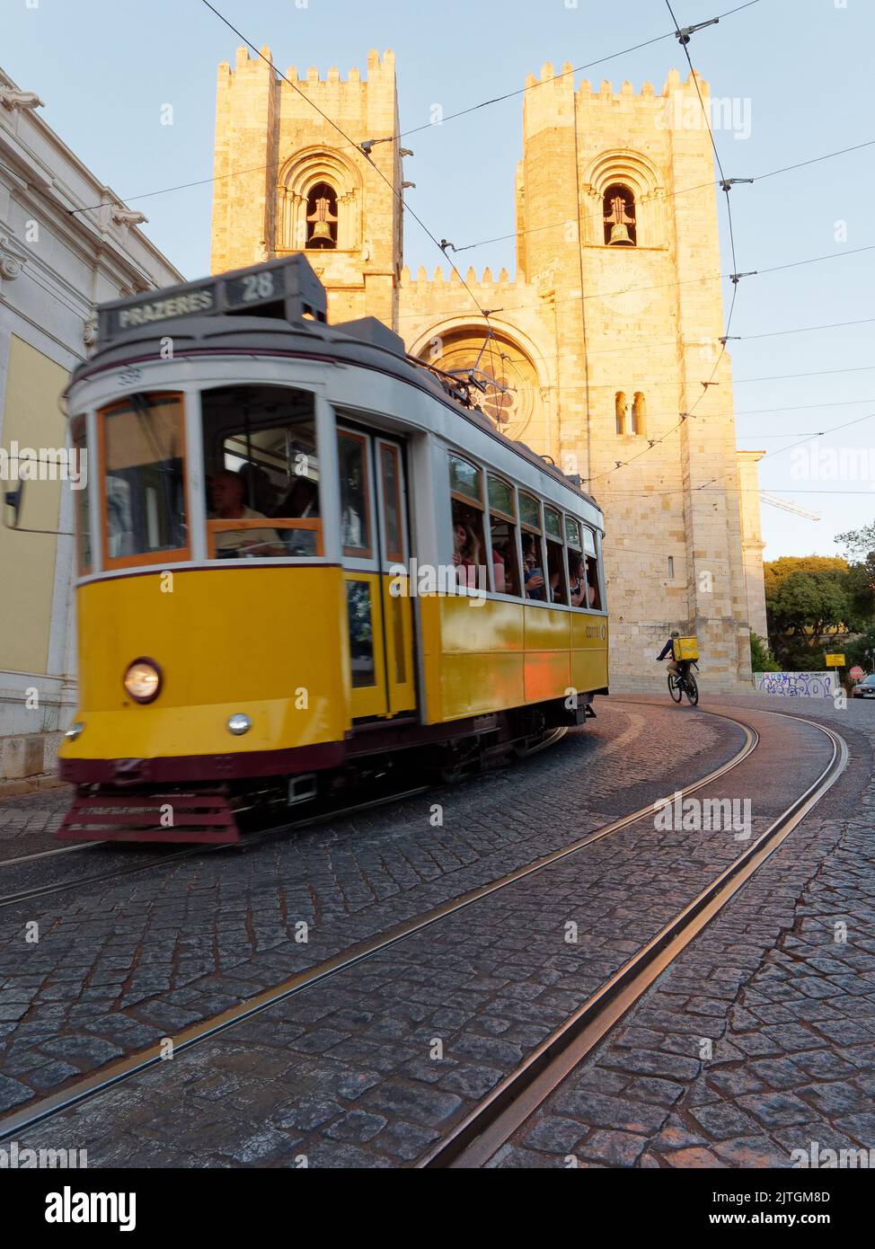 La cathédrale Saint Mary Major alias la cathédrale de Lisbonne (Sé de Lisboa) en tant que tramway jaune et cycliste de livraison passe un soir d'été. Banque D'Images