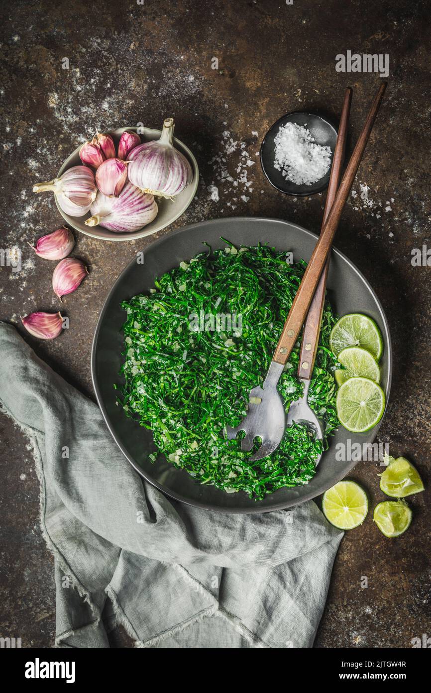 Rubans de colverts sautés dans un plat de service avec ustensiles de service, tranches d'ail et de lime Banque D'Images