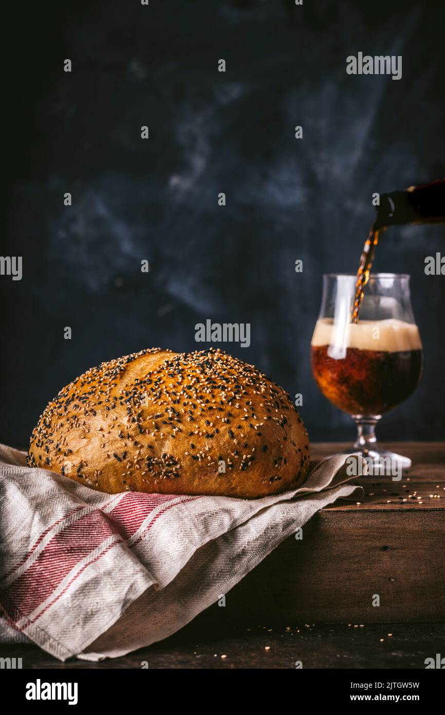Pain rond de poppyseed pain avec bière foncée dans le verre et la bière verser action Banque D'Images