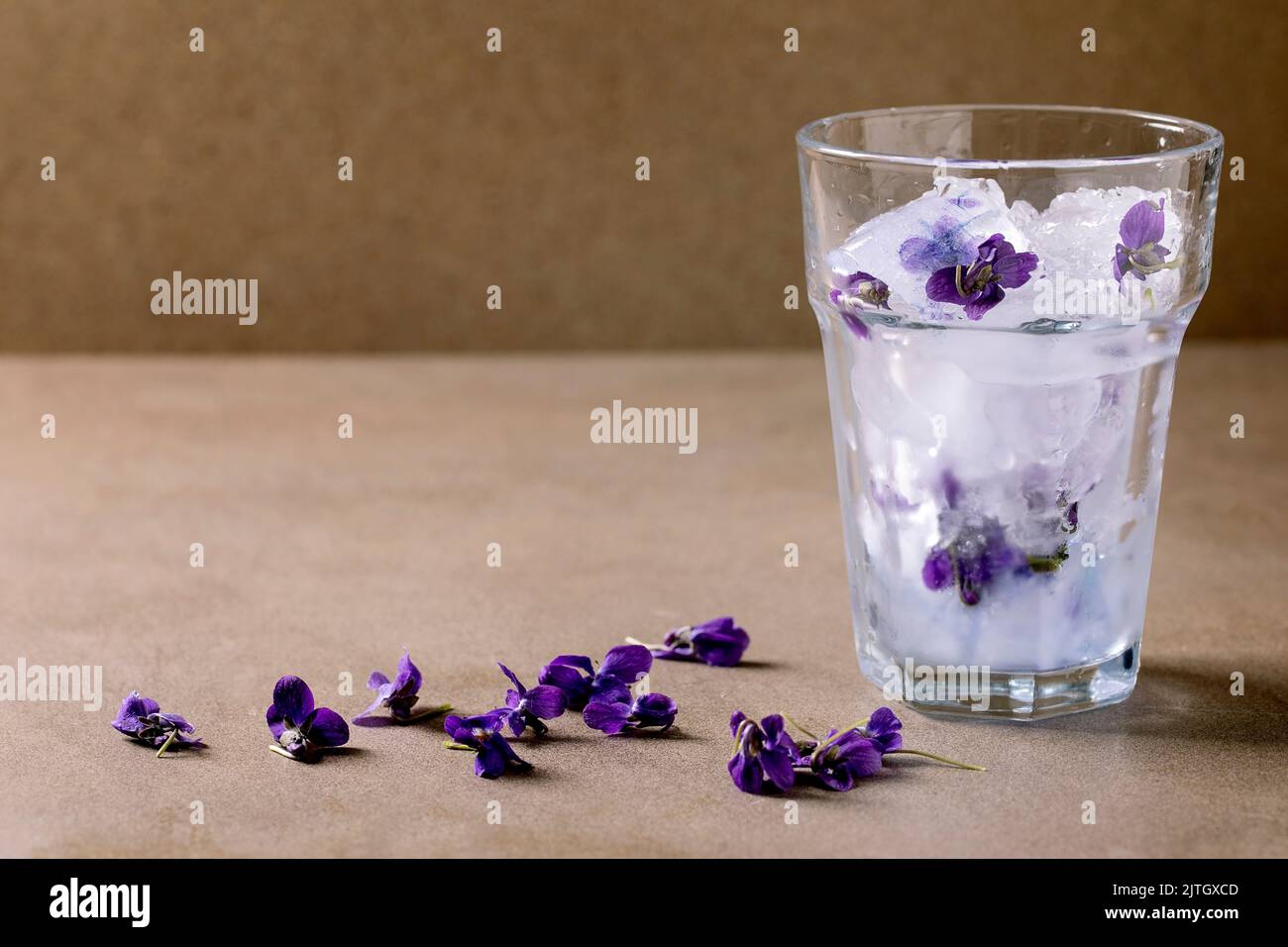 Verre transparent de violettes fleur glace concassée pour faire froid boisson de rafraîchissement d'été cocktail de soda de limonade. Debout sur une table brune. Copier l'espace Banque D'Images