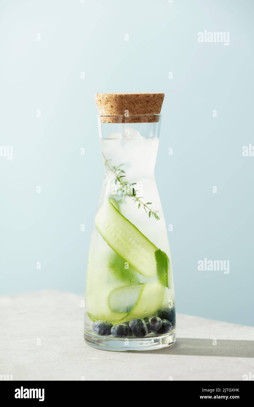 Boisson d'été dans une bouteille avec concombre, mûre et romarin sur fond bleu ciel Banque D'Images