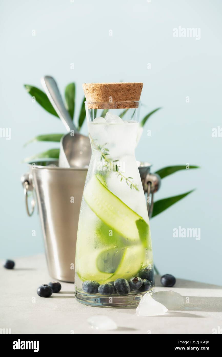 Eau d'été infusée avec concombre, mûre et romarin et seau à glace sur fond bleu ciel Banque D'Images