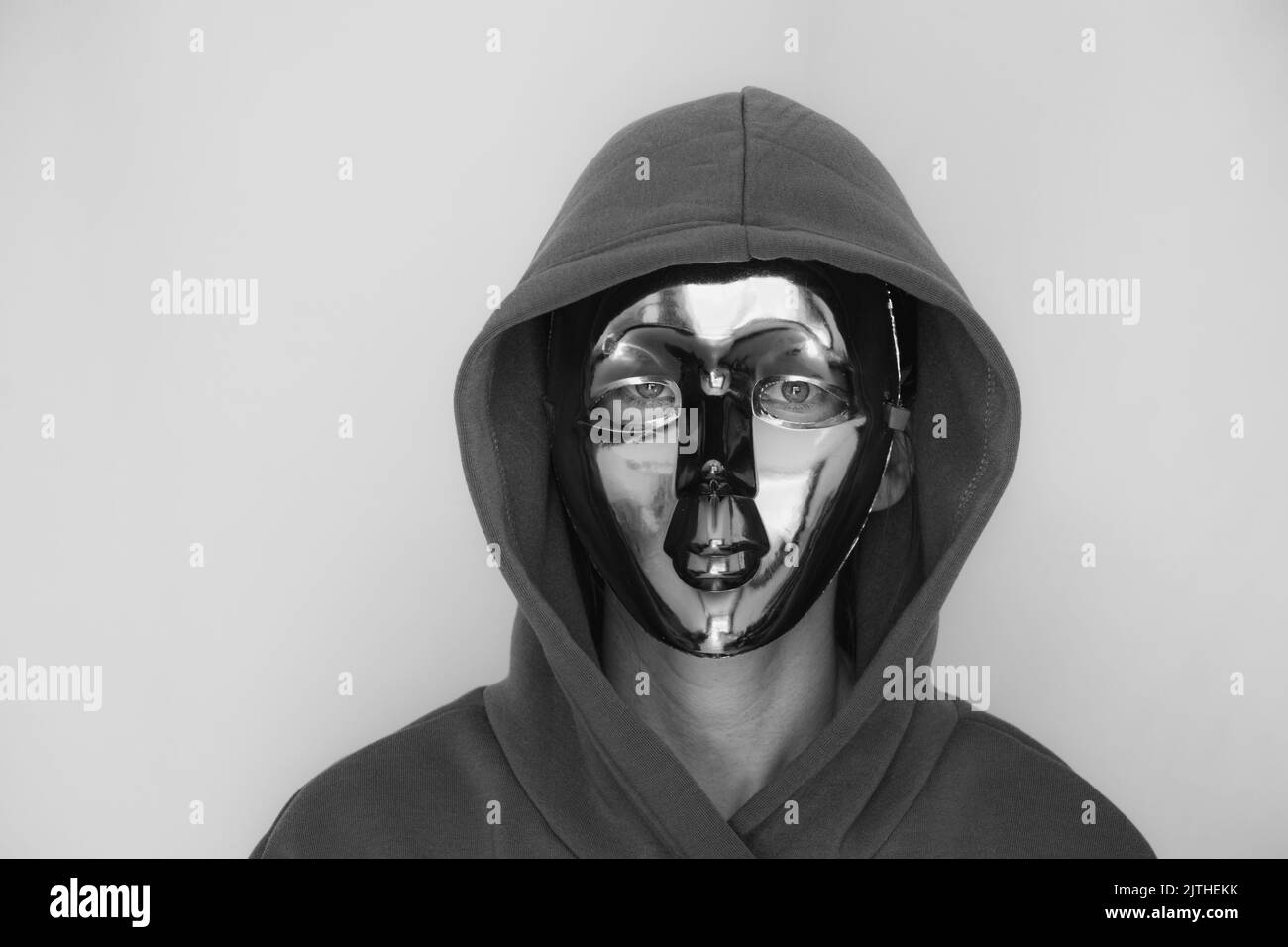 Une fille dans un masque en plastique et dans une cagoule sur un fond isolé, l'anonymat, cacher son visage Banque D'Images