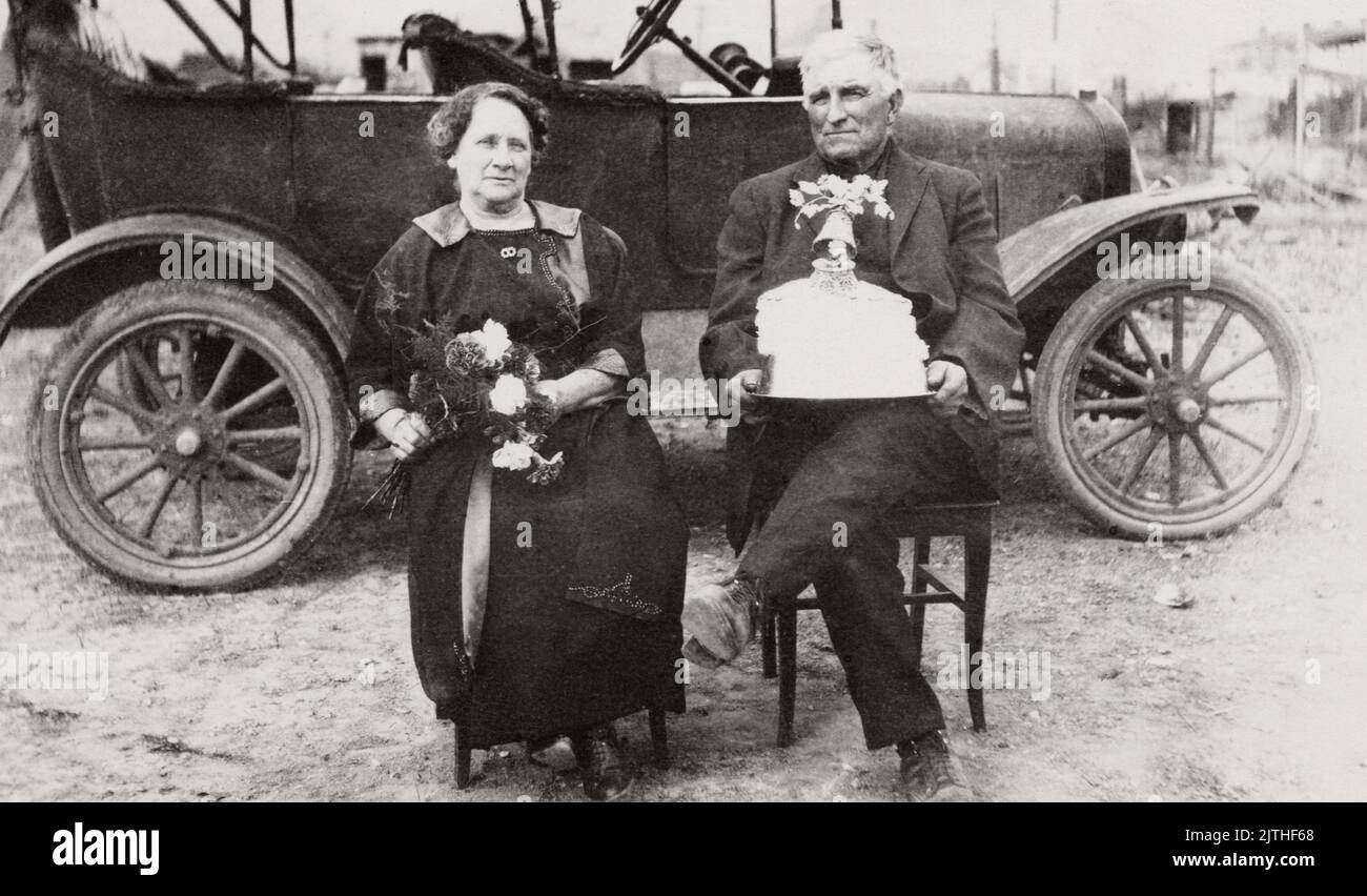 Couple plus âgé avec gâteau et automobile, emplacement inconnu, environ 1905-1915 carte postale. Photographe non identifié Banque D'Images