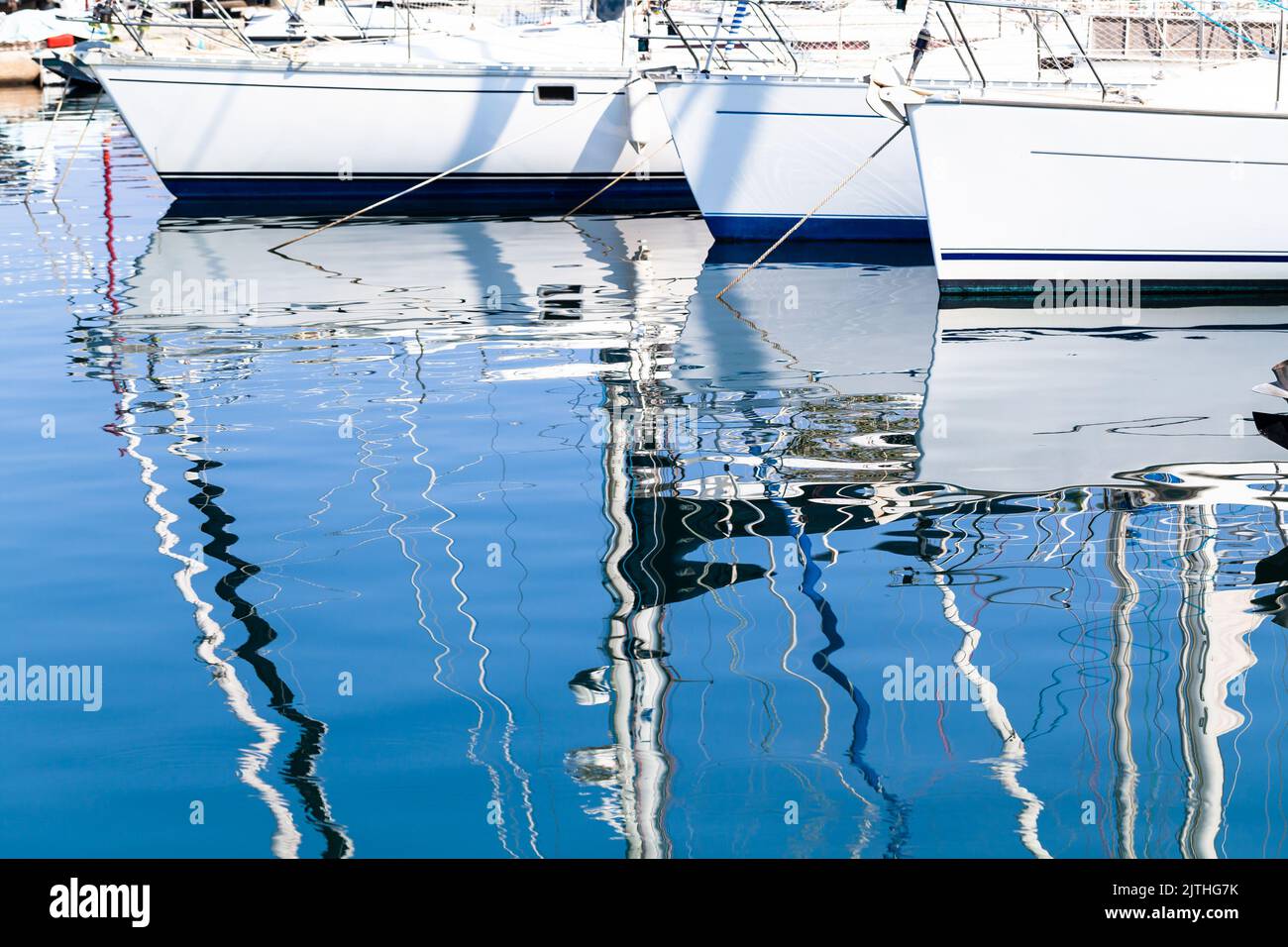Les yachts à voile amarrés dans la marina par une journée ensoleillée se reflètent dans l'eau de mer ondulée. Photo d'arrière-plan abstraite Banque D'Images