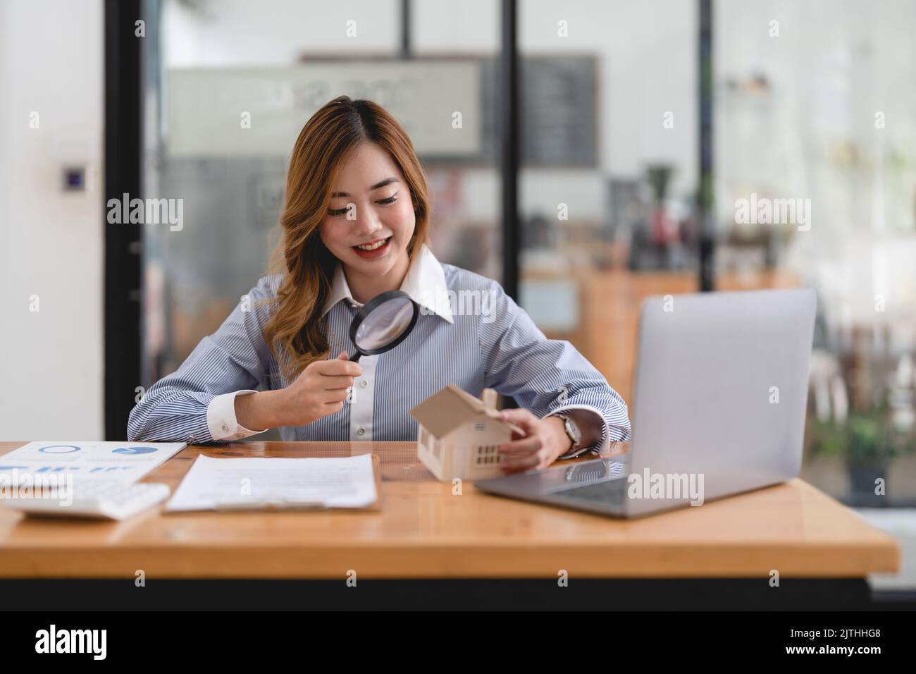 Recherche d'agence immobilière, d'assurance de biens, de prêt hypothécaire ou de maison neuve. Femme avec loupe sur une maison en bois à son bureau Banque D'Images