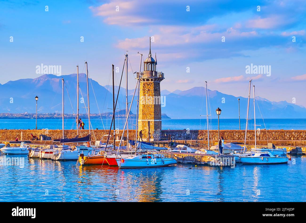 La soirée brumeuse sur le lac de Garde avec des yachts, le phare de Faro et les silhouettes de Garda Prealps en arrière-plan, Desenzano del Garda, Lombardie, Italie Banque D'Images