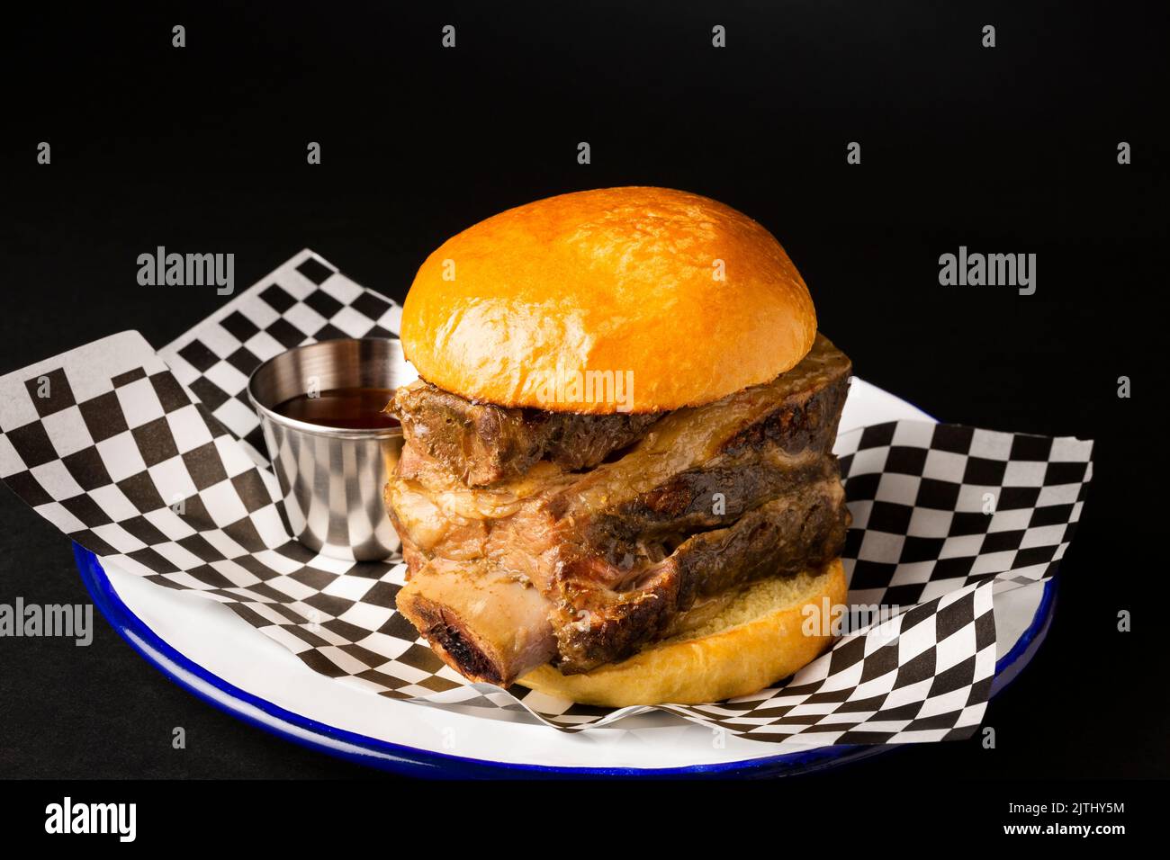 Hamburger avec côtes de bœuf sur une assiette blanche sur fond noir Banque D'Images