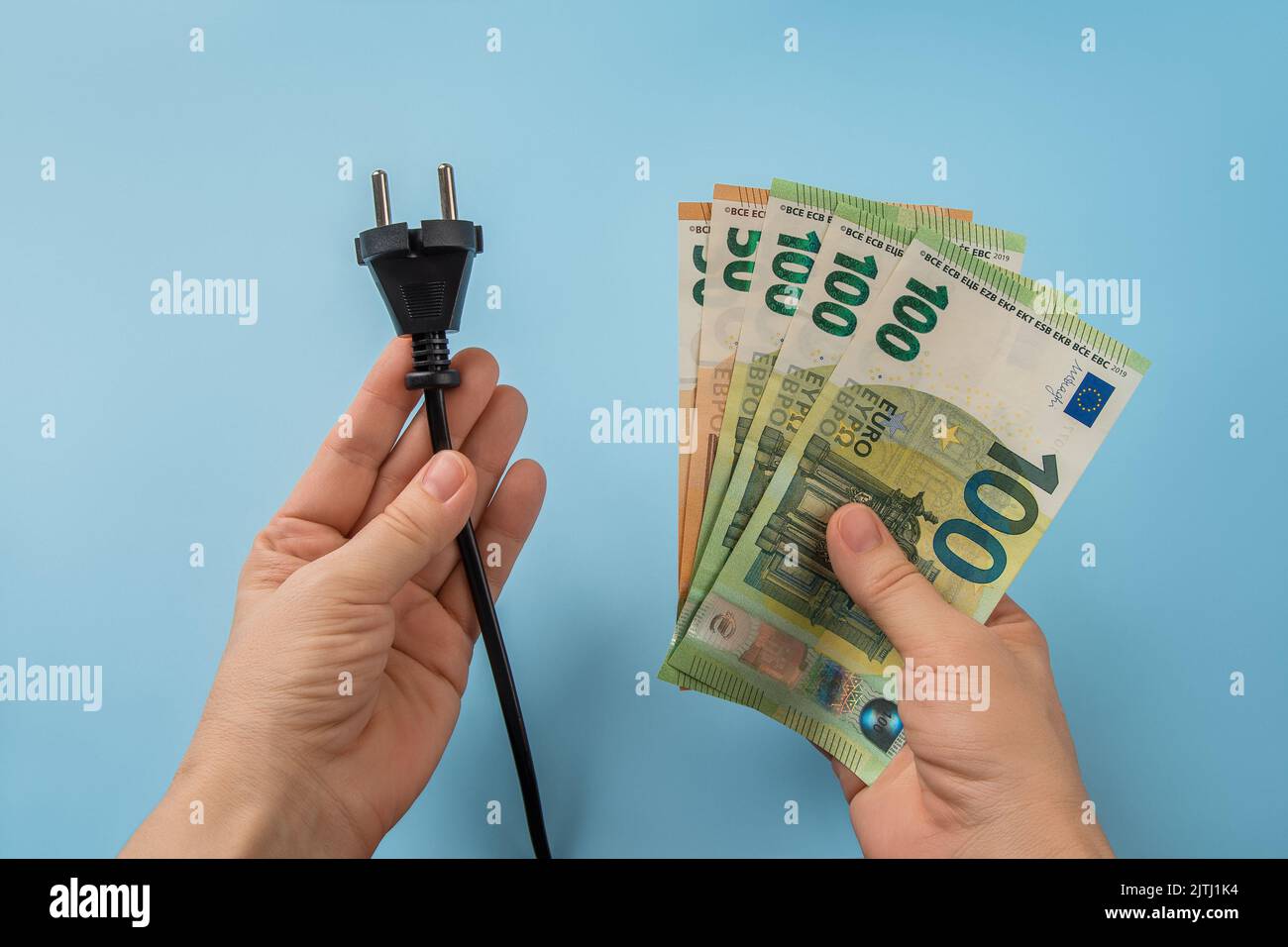 Les mains de la femme tiennent la fiche électrique et les billets en euros sur fond bleu. Coûts énergétiques élevés en Europe. La facture électrique augmente le concept. Hausse du prix de l'énergie. Banque D'Images
