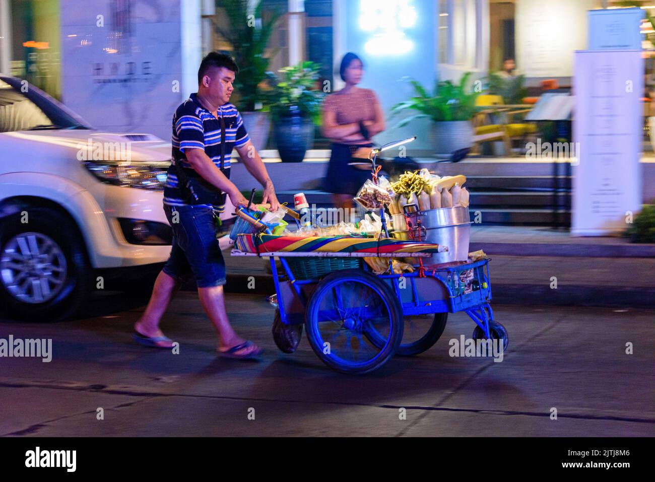 L'homme pousse un chariot contenant de l'équipement pour lui permettre de cuisiner de la nourriture de rue le long d'une rue à Bangkok Banque D'Images