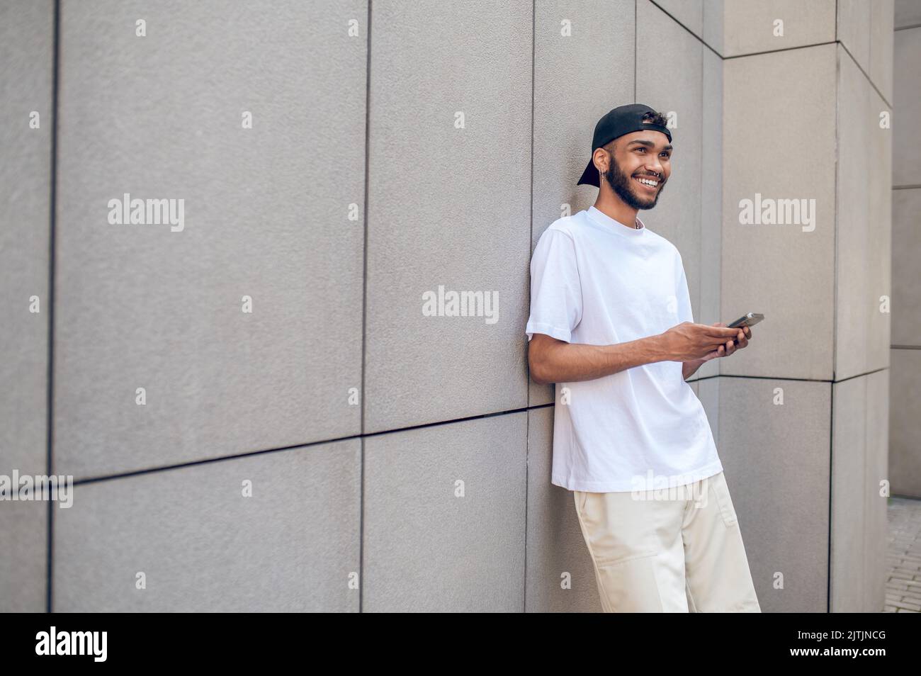 Jeune homme en chemise blanche et casquette noire debout près du mur et  attendant quelqu'un Photo Stock - Alamy