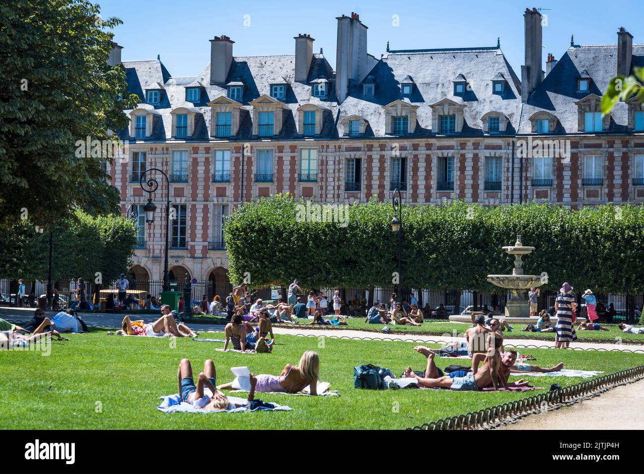 Personnes se détendant dans le parc central de la place des Vosges, la plus ancienne place planifiée de Paris, construite au 17th siècle dans le quartier du Marais, par Banque D'Images