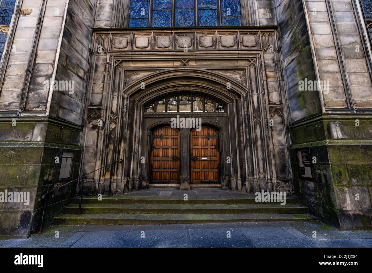 Une ancienne cathédrale en pierre avec deux portes en bois entourée de fenêtres en pierre et en vitraux Banque D'Images