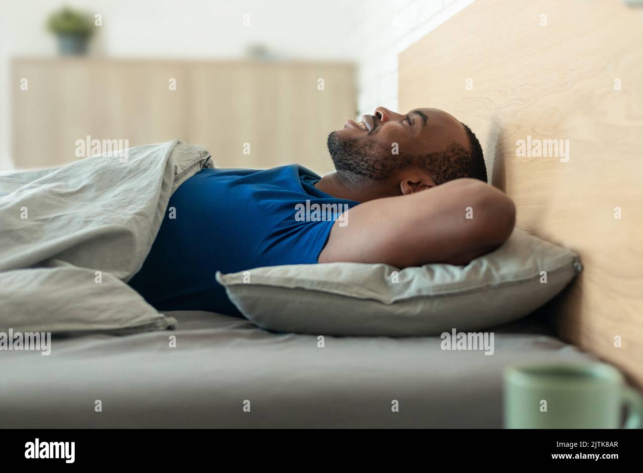 Homme noir allongé dans le lit tenant les mains derrière la tête intérieure Banque D'Images