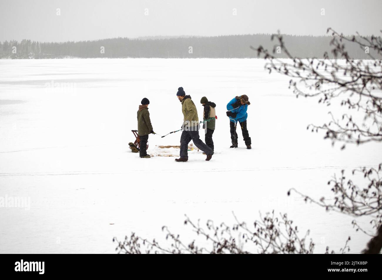 Hommes matures avec des fils utilisant la tarière de glace pour la pêche au lac gelé Banque D'Images