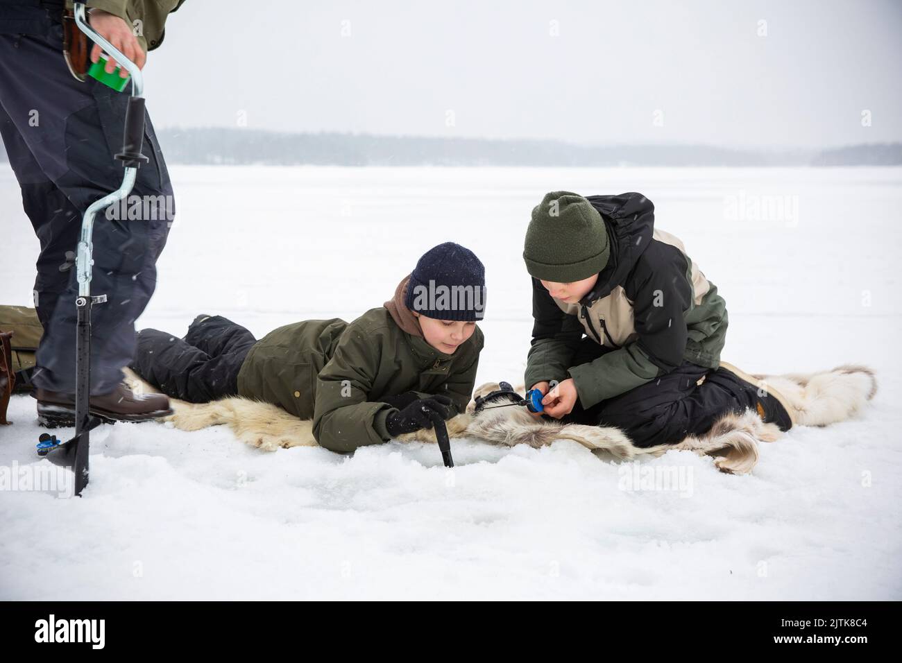 Garçons en vêtements chauds pêche sous la glace au lac gelé pendant les vacances Banque D'Images
