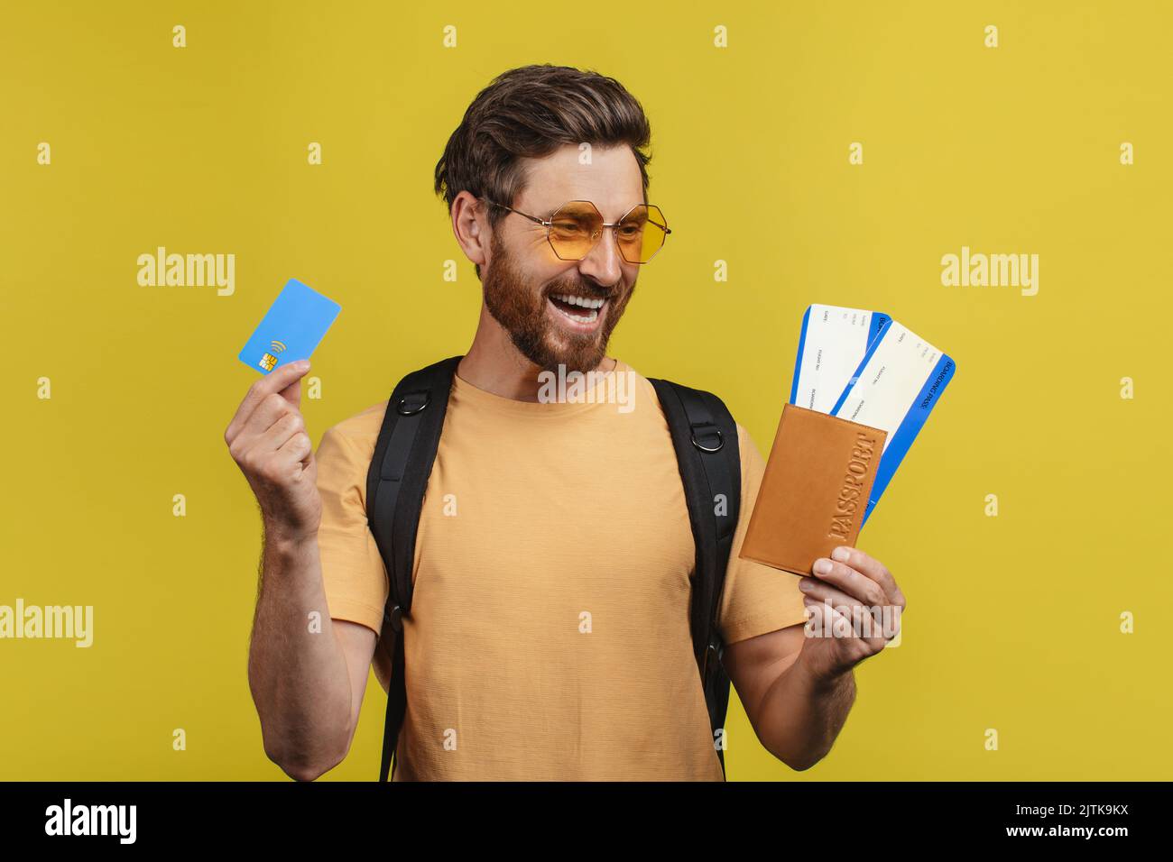 Budget de voyage pour les voyages à l'étranger. Joyeux touriste mâle avec carte de crédit, passeport et billets posant sur fond jaune Banque D'Images