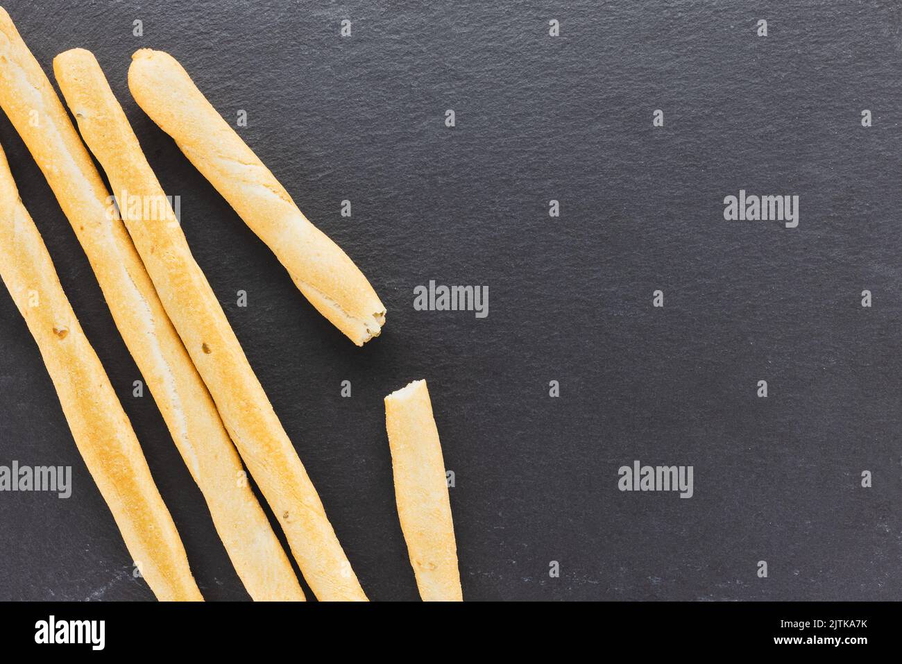 Gressins italiens frais Grissini servis sur fond noir. Pain cuit à sec avec des morceaux d'olive sur une assiette d'ardoise. Vue de dessus, espace de copie Banque D'Images