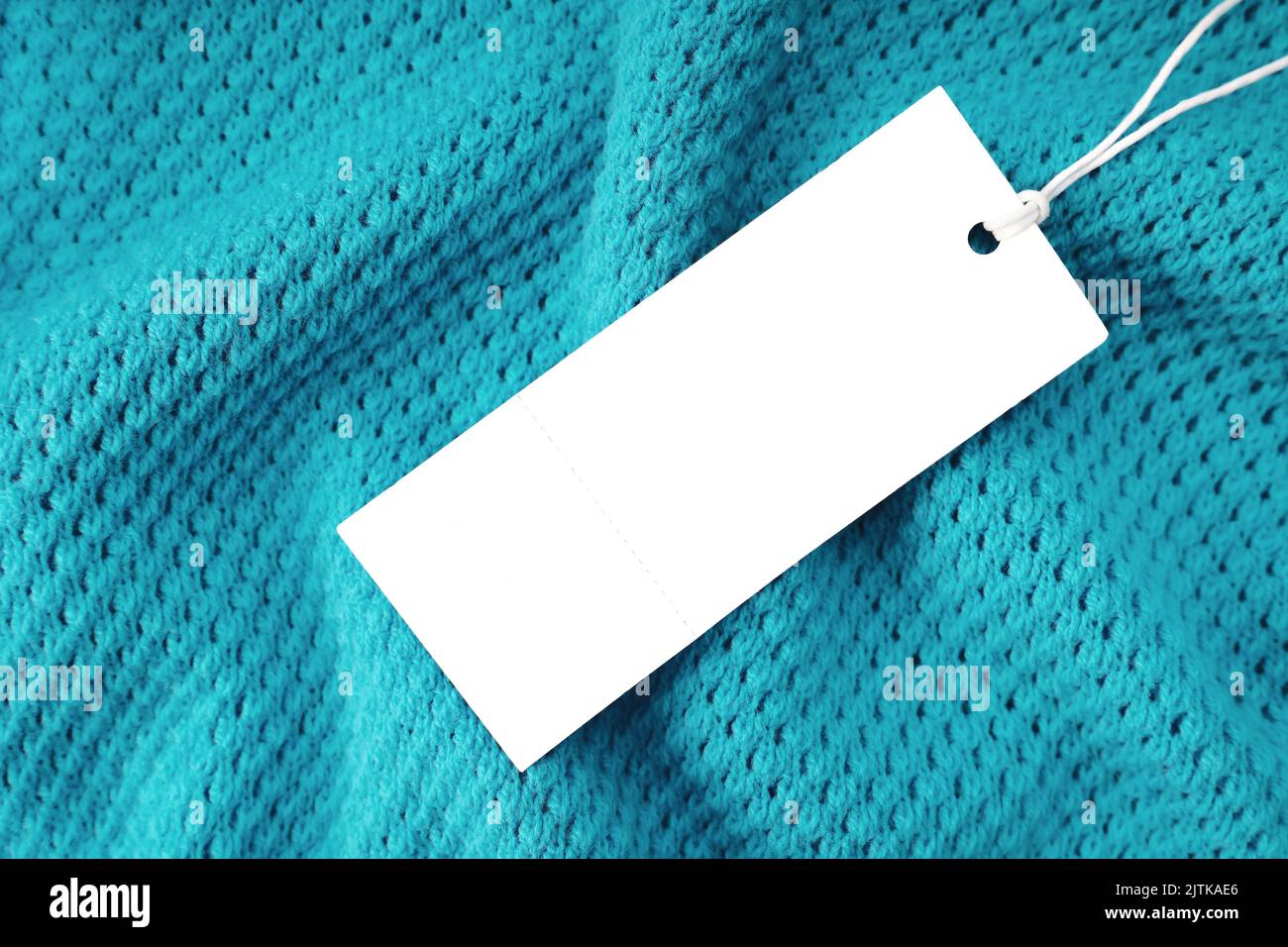 Blanc blanc vierge rectangulaire étiquette de vêtements, modèle de maquette d'étiquette sur fond de tissu tricoté turquoise . Étiquette de prix avec espace pour le texte. Shoppin Banque D'Images