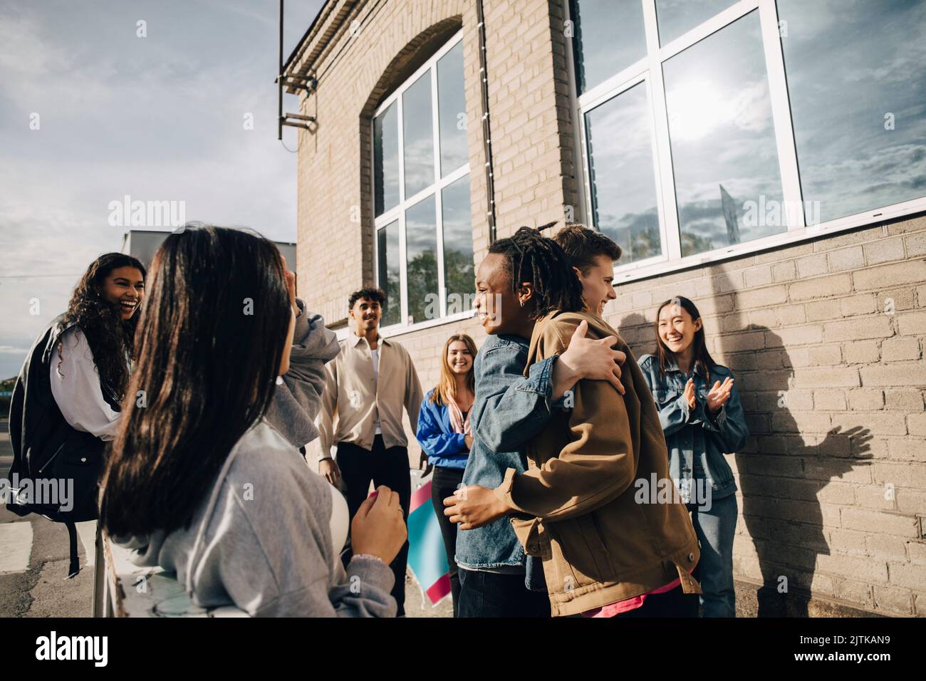 Jeune homme souriant embrassant une femme par des amis à l'extérieur du bâtiment Banque D'Images