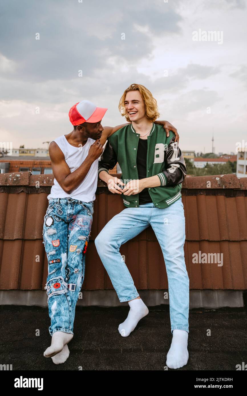 Pleine longueur de jeunes hommes heureux debout sur le toit contre ciel nuageux Banque D'Images