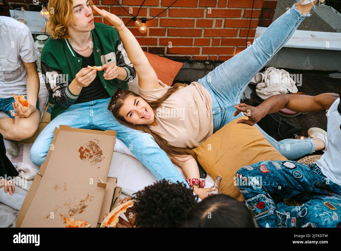 Portrait d'une femme heureuse qui colle à la langue tout en étant couché par des amis qui mangent de la pizza sur le toit Banque D'Images