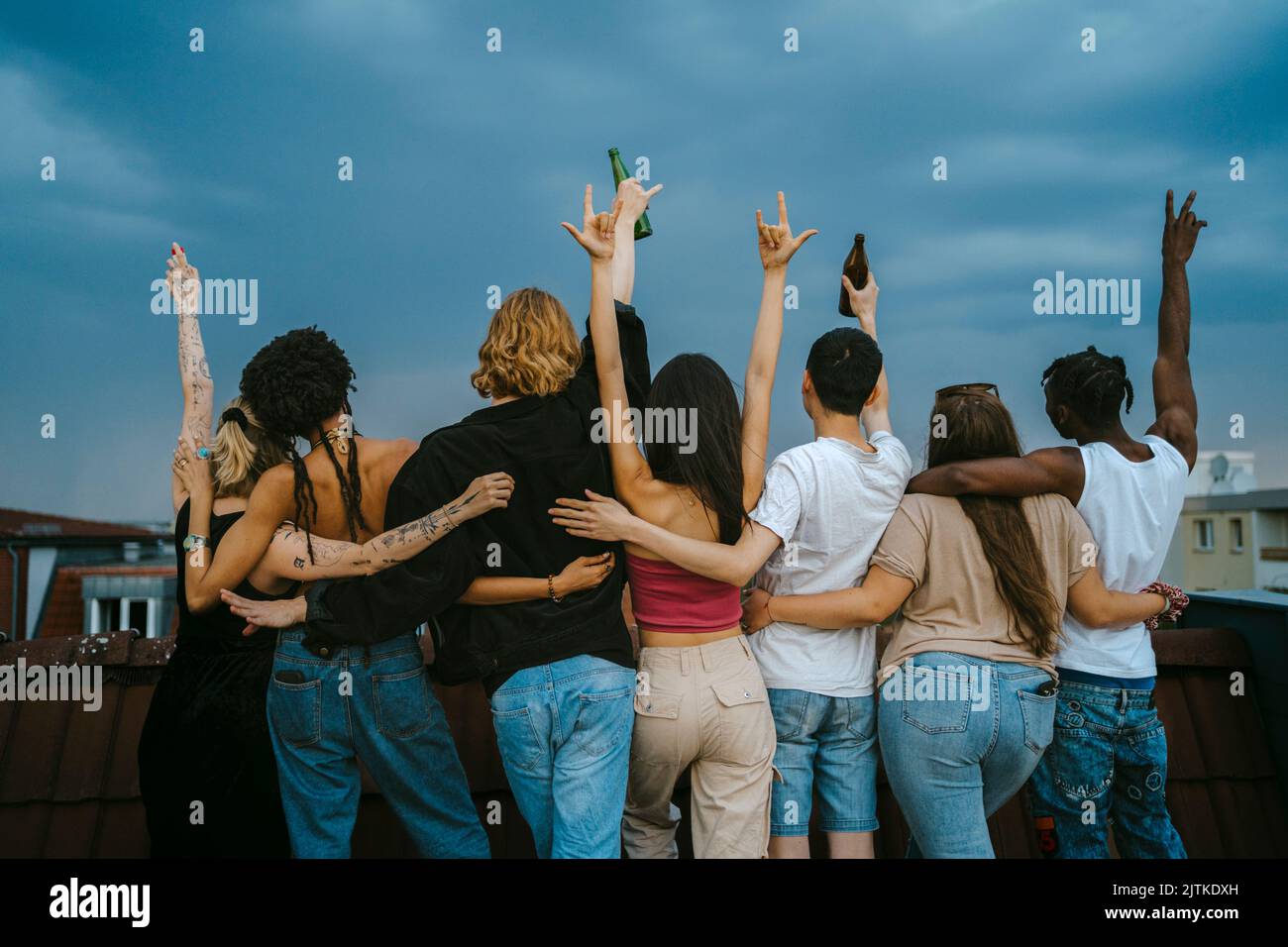 Vue arrière des jeunes hommes et femmes multiraciaux qui gestuelle avec les bras levés sur le toit au crépuscule Banque D'Images