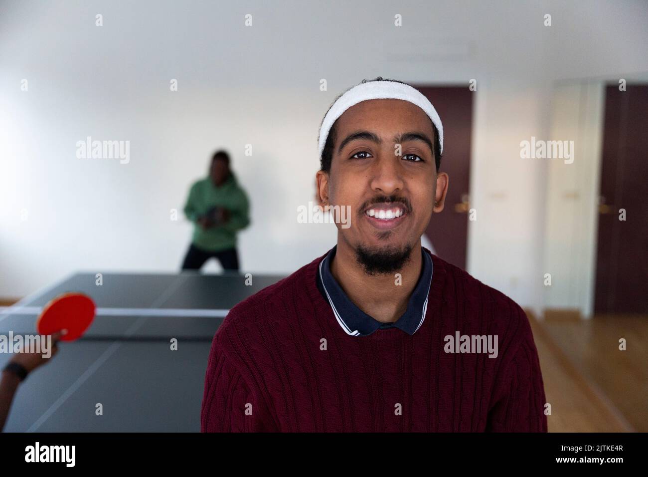 Homme souriant avec des amis jouant au tennis de table en arrière-plan dans la salle de jeux Banque D'Images