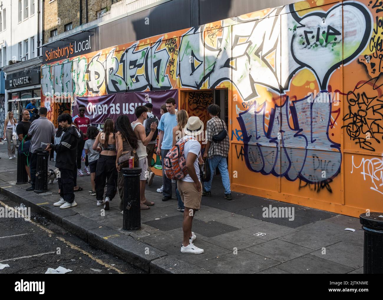 Les gens font la queue devant un magasin couvert de Graffiti, pendant le Notting Carnival Weekend, West London, 2022. Banque D'Images