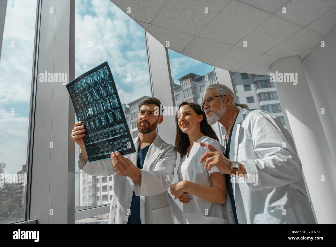 Les médecins collègues regardent et discutent de rayons X ou d'IRM de la colonne vertébrale du patient dans la clinique médicale Banque D'Images