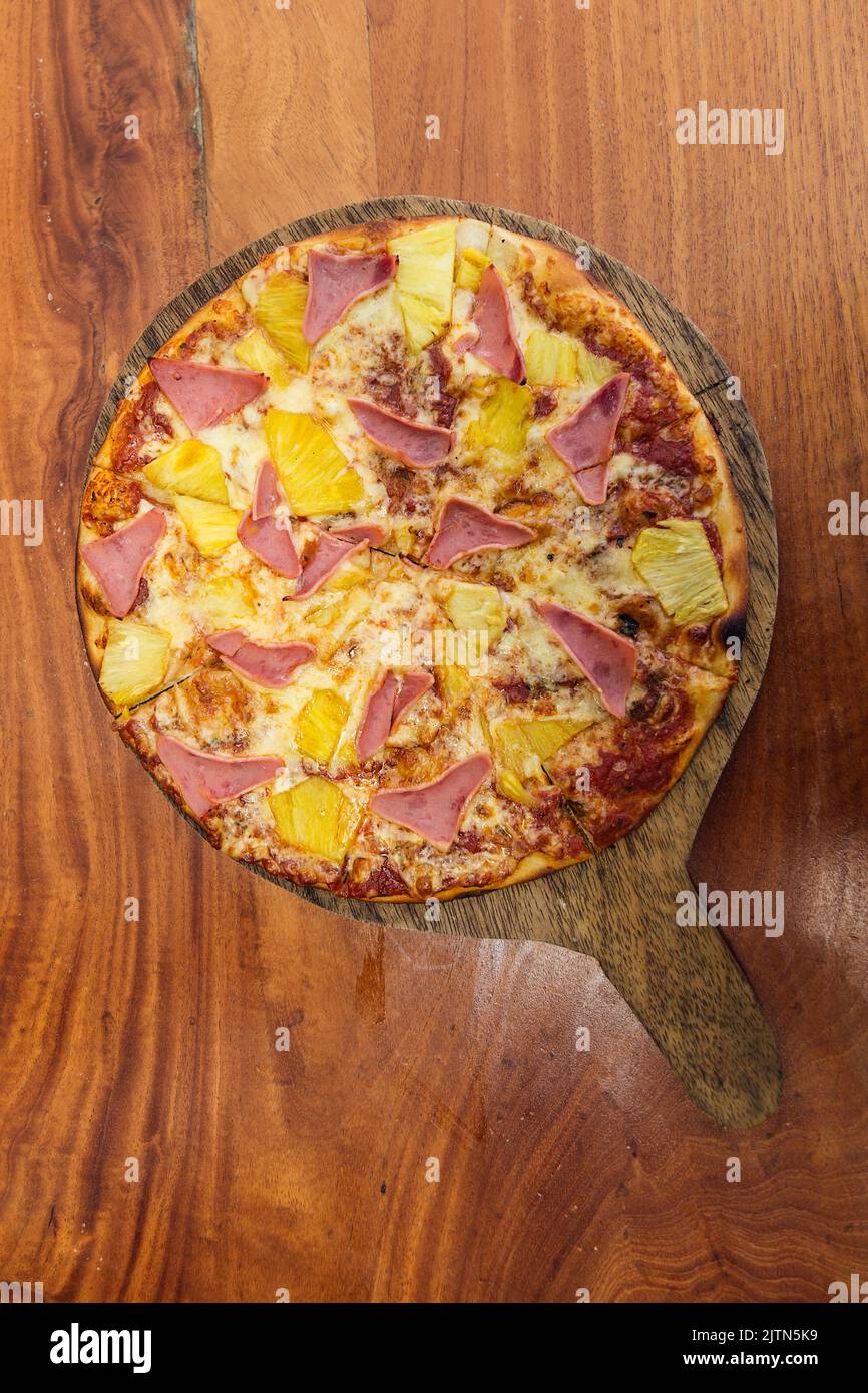 Pizza hawaïenne au fromage, au jambon et à l'ananas, servie sur une planche de bois dans un restaurant italien. Banque D'Images