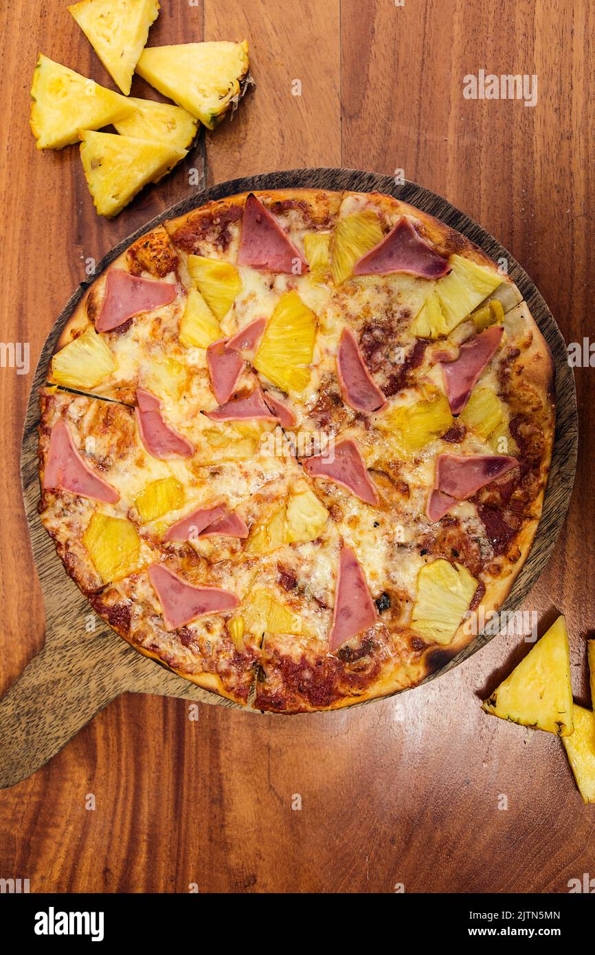 Pizza hawaïenne au fromage, au jambon et à l'ananas, servie sur une planche de bois dans un restaurant italien. Banque D'Images