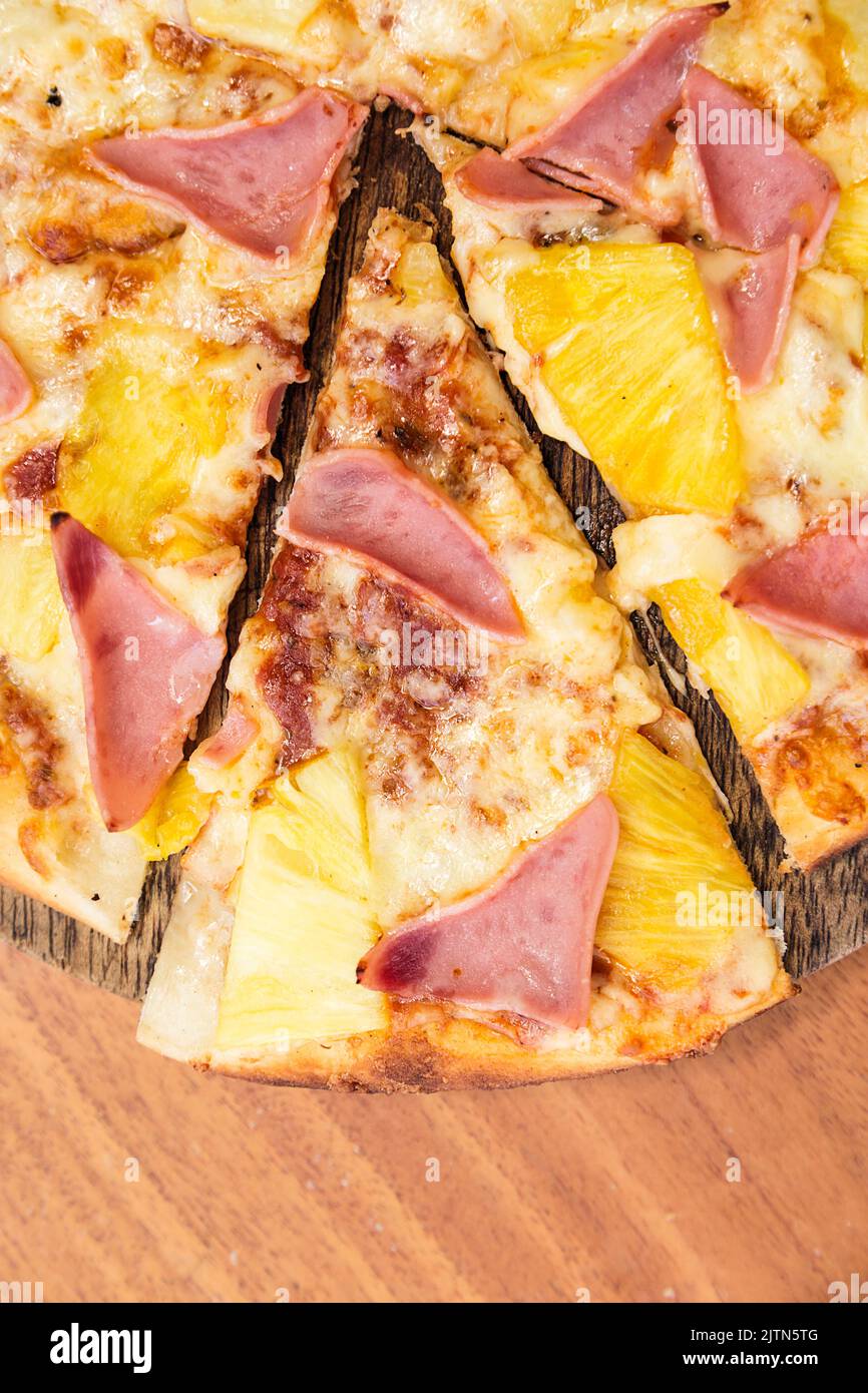 Pizza hawaïenne au fromage, au jambon et à l'ananas, servie sur une planche de bois dans un restaurant italien. Banque D'Images