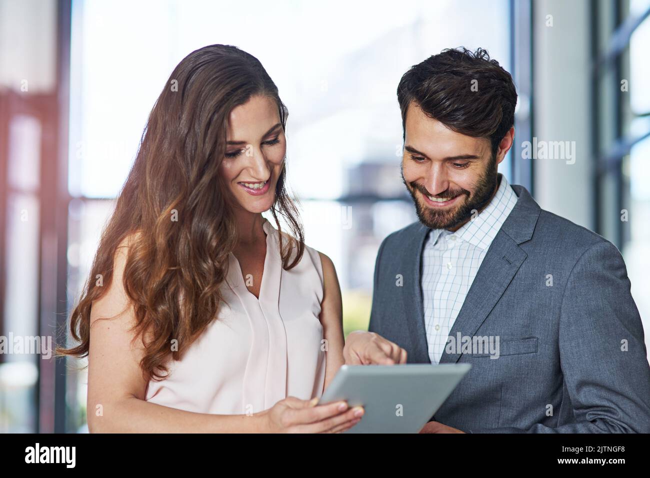 Des collaborations sans câble. Un jeune homme d'affaires et une femme d'affaires utilisant une tablette numérique ensemble dans un bureau. Banque D'Images