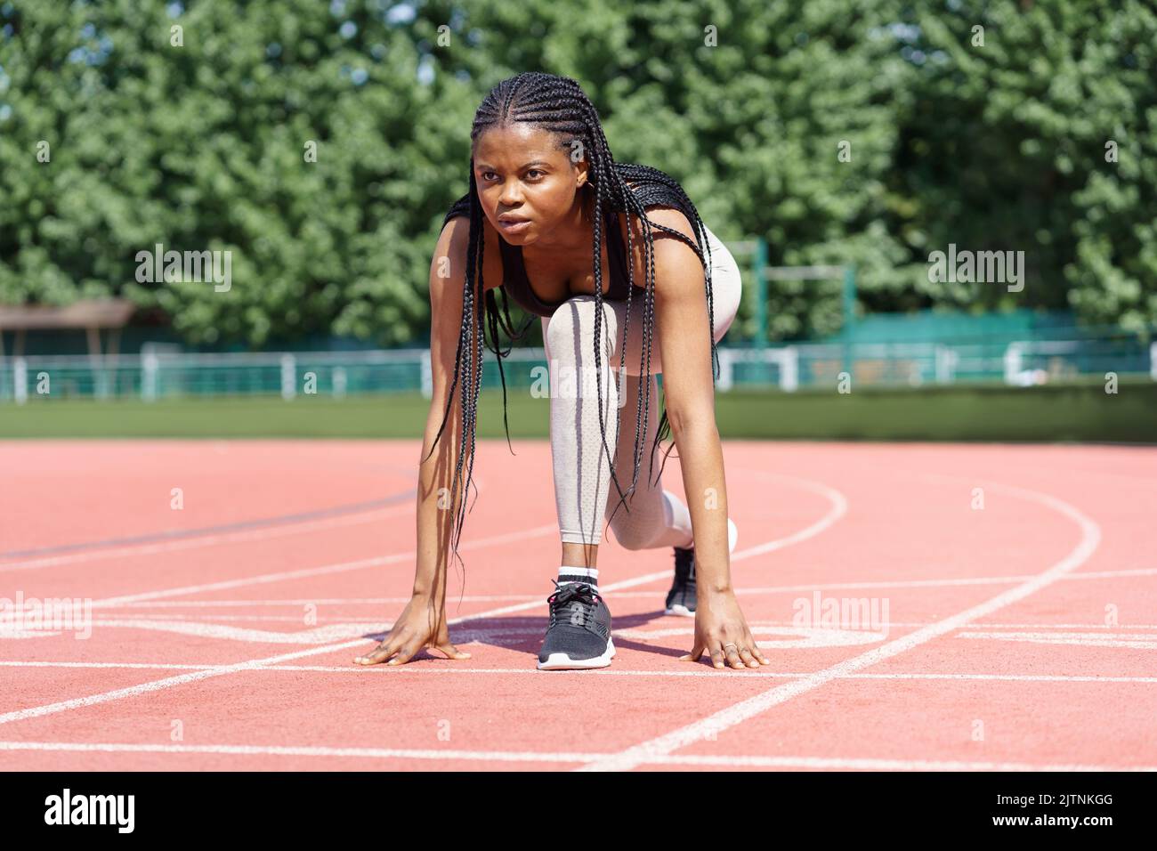 Une femme afro-américaine aux longues tresses prépare une course à pied à bas régime sur la piste rouge du stade Banque D'Images