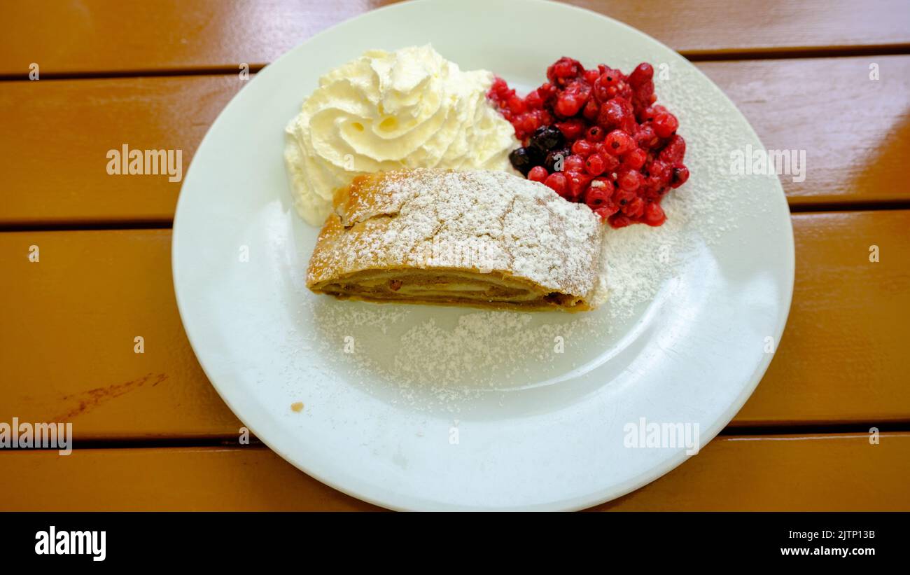 Strudel aux baies maison en tranches, servi avec des raisins de Corinthe rouges frais et du sucre en poudre sur une assiette de crème fouettée Banque D'Images
