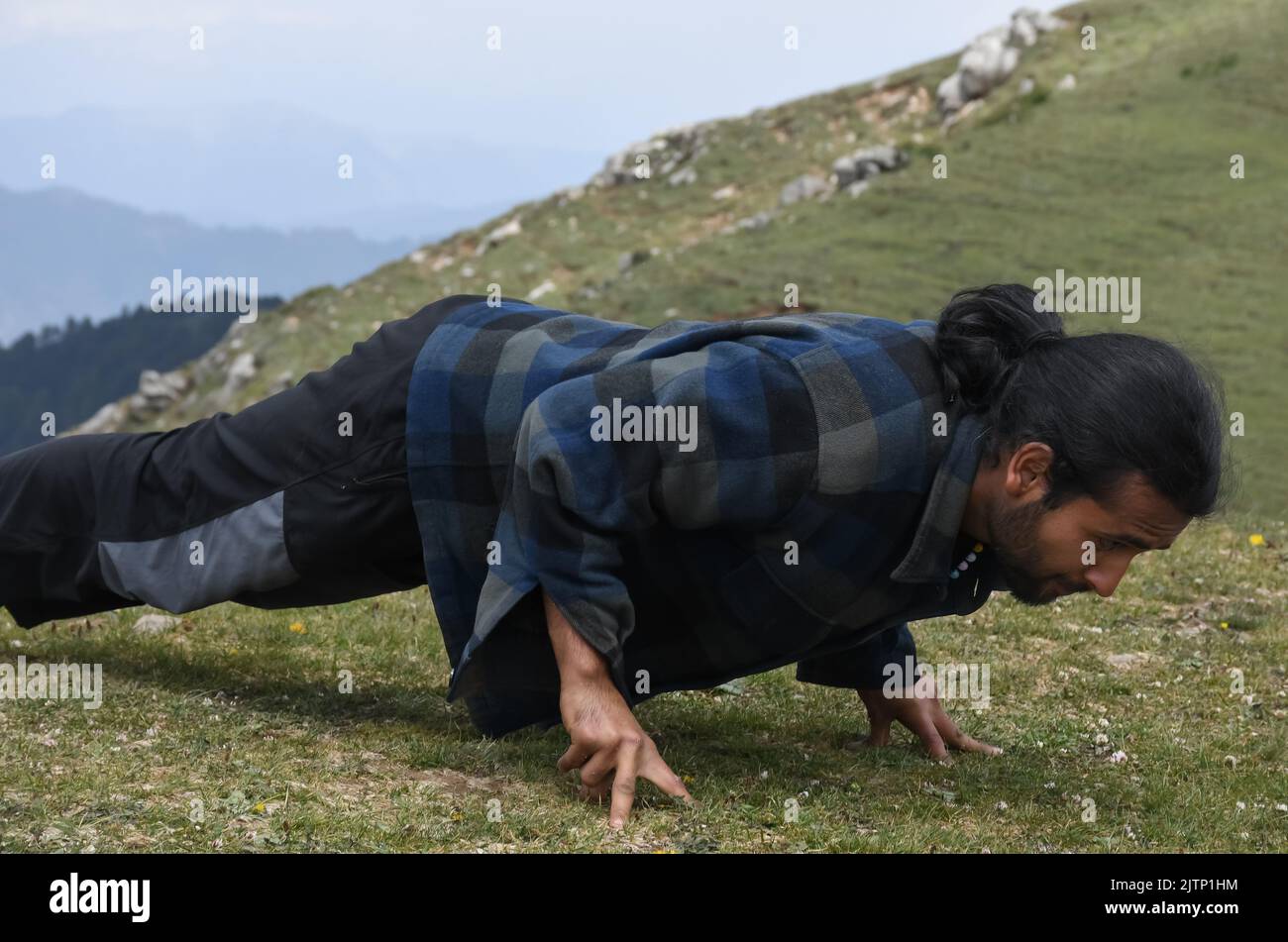 Un beau jeune indien aux cheveux longs faisant des push-up avec trois doigts en haut de la montagne Banque D'Images