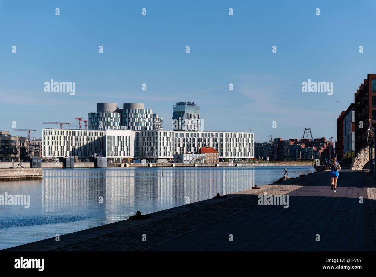 Copenhague, Danemark. 13 août 2022. Femme jogging à côté de la rivière à Copenhague avec des bâtiments de la ville des Nations Unies en arrière-plan Banque D'Images
