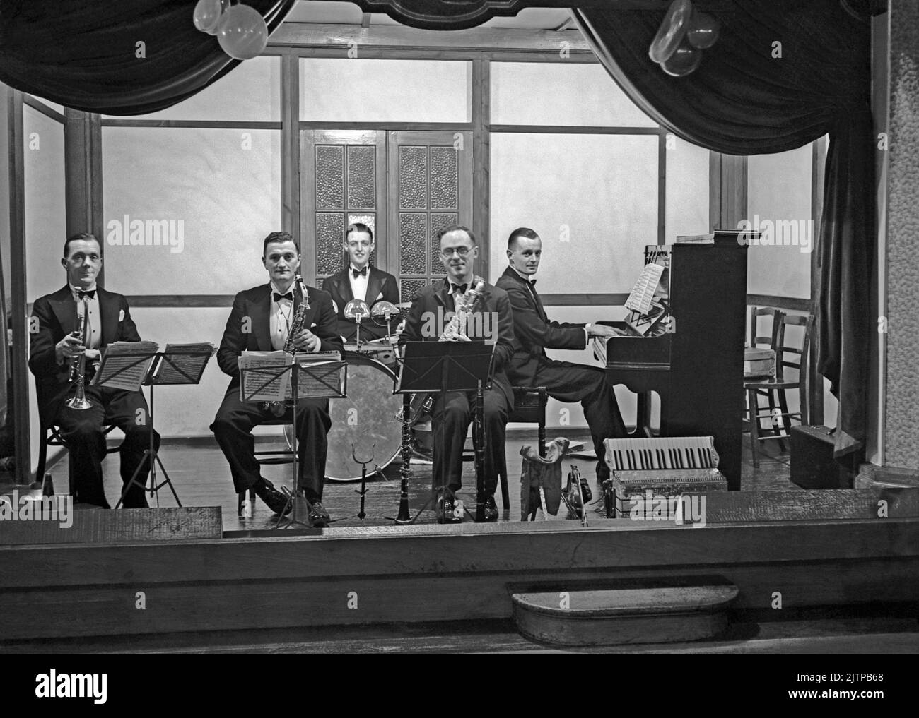 Un groupe de danse britannique de cinq pièces, Jack Monks Jazz Band, sur scène à Sutton, Surrey (aujourd'hui un quartier de Londres), au Royaume-Uni, en décembre 1937. Les premiers groupes de danse et de swing ont eu leur âge d'or au Royaume-Uni durant la période 1920s-30s. Groupes joués dans les salles de danse et les salles de bal de l'hôtel. Ils jouaient de la musique mélodique et de bon temps et des joueurs individuels joueraient dans plusieurs groupes. Cette image provient d'un vieux négatif en verre – une photographie vintage de 1930s. Banque D'Images Un groupe de danse britannique de cinq pièces, Jack Monks Jazz Band, sur scène à Sutton, Surrey (aujourd'hui un quartier de Londres), au Royaume-Uni, en décembre 1937. Les premiers groupes de danse et de swing ont eu leur âge d'or au Royaume-Uni durant la période 1920s-30s. Groupes joués dans les salles de danse et les salles de bal de l'hôtel. Ils jouaient de la musique mélodique et de bon temps et des joueurs individuels joueraient dans plusieurs groupes. Cette image provient d'un vieux négatif en verre – une photographie vintage de 1930s. Banque D'Images