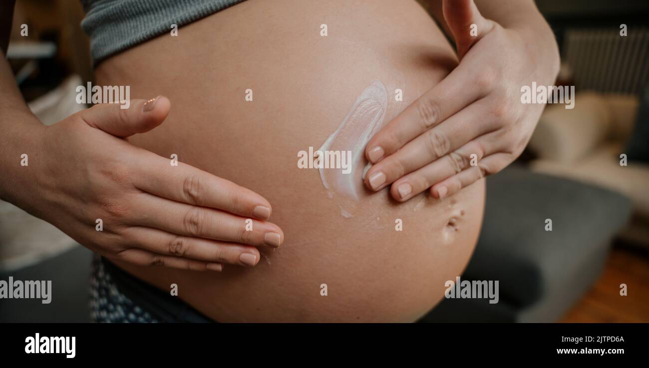 Gros plan femme enceinte frottant doucement dans la crème sur son ventre Banque D'Images