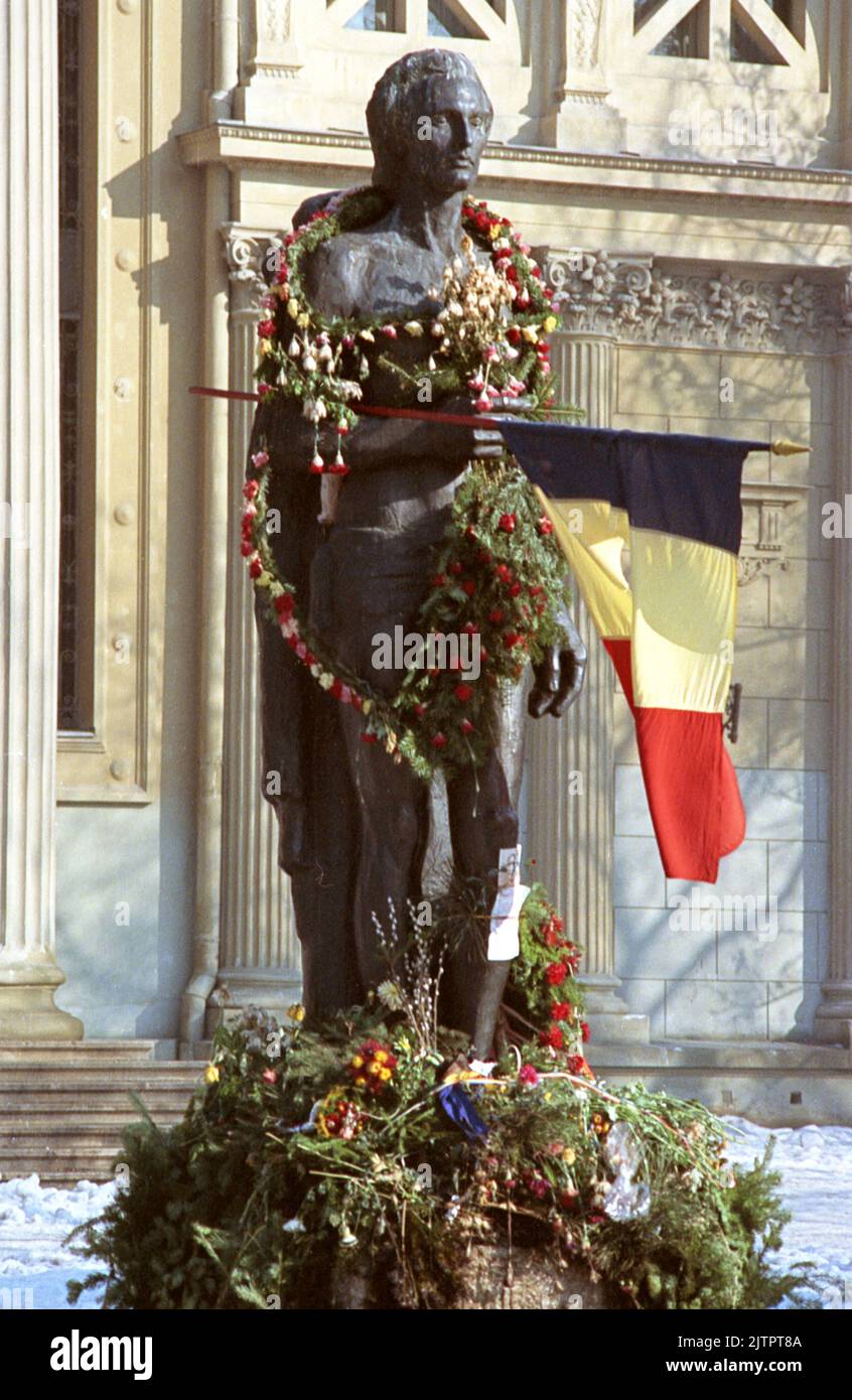 Bucarest, Roumanie, janvier 1990. Quelques semaines après la révolution roumaine de 1989, des fleurs sont placées autour de la statue du poète national Mihai Eminescu, devant l'Athenaeum. Le drapeau national avec l'emblème socialiste coupé est devenu un symbole pendant la révolution, représentant la fin de l'ère communiste. Banque D'Images