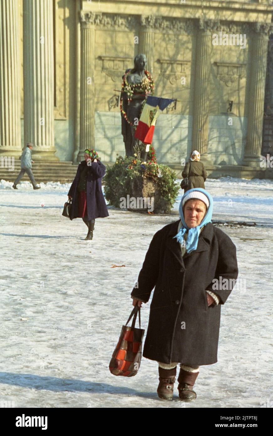 Bucarest, Roumanie, janvier 1990. Quelques semaines après la révolution roumaine de 1989, des fleurs sont placées autour de la statue du poète national Mihai Eminescu, devant l'Athenaeum. Le drapeau national avec l'emblème socialiste coupé est devenu un symbole pendant la révolution, représentant la fin de l'ère communiste. Banque D'Images