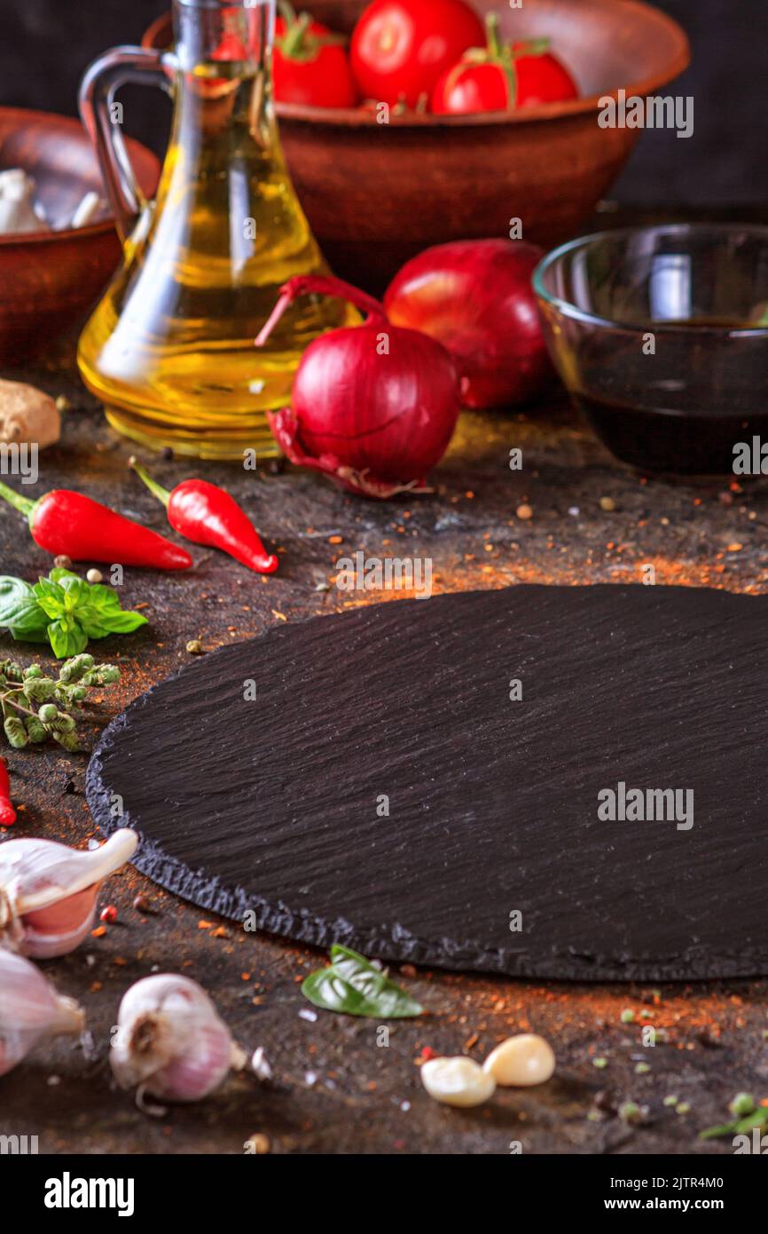 Décor culinaire avec table ronde en ardoise, huile d'olive dans une carafe et légumes.Espace vide pour le menu ou la recette avec mise au point sélective Banque D'Images