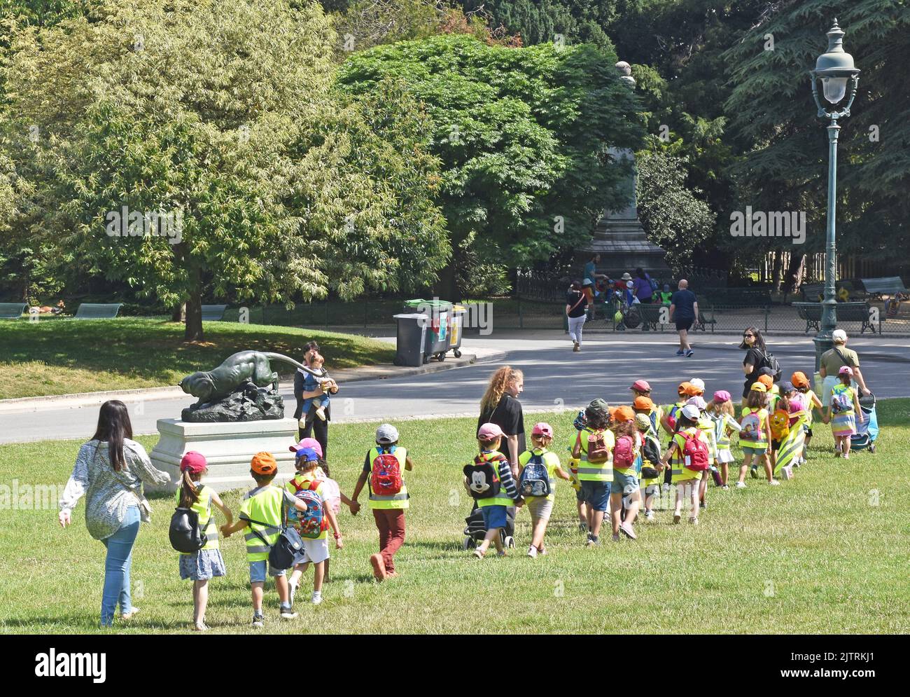 Une classe de jeunes enfants bercés par deux dans le parc Montsouris, à Paris, qui tiennent tous les mains et portent des dorures et des casquettes de baseball à haute visibilité Banque D'Images