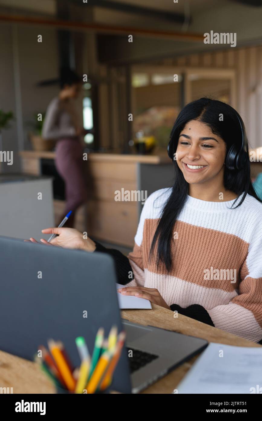 Jeune fille biraciale souriante portant un casque et parlant sur un ordinateur portable pendant une conférence en ligne Banque D'Images