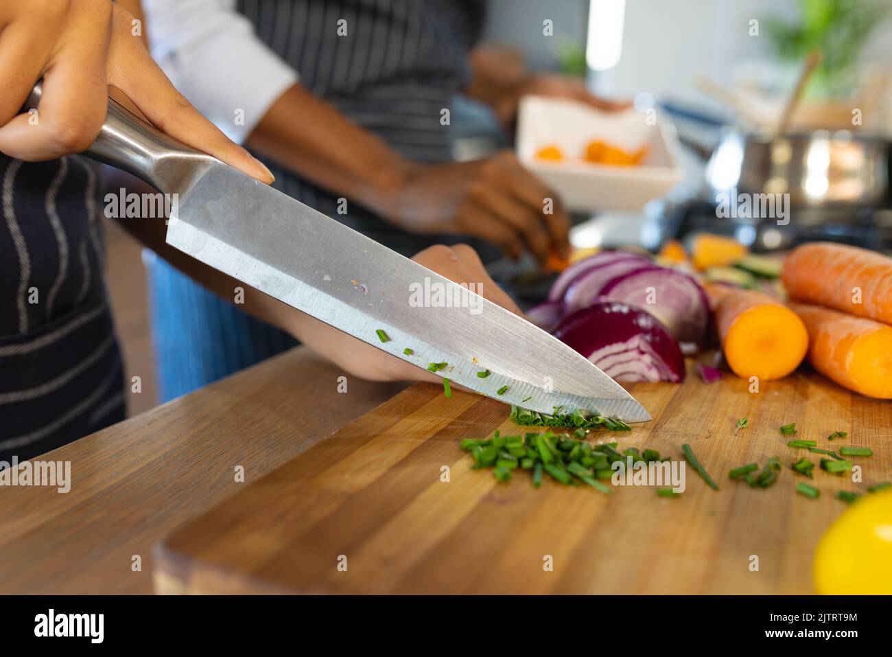 Section centrale de la fille biraciale et la mère coupant des légumes frais sur la planche à découper dans la cuisine Banque D'Images