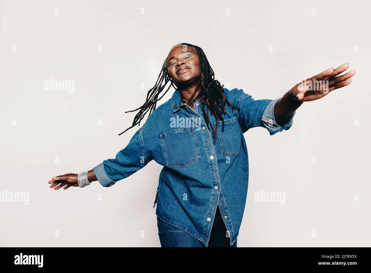 Femme blissful s'amusant dans le studio. Femme insouciante avec des dreadlocks debout avec ses yeux fermés et ses bras étirés. Bonne femme mature nous Banque D'Images